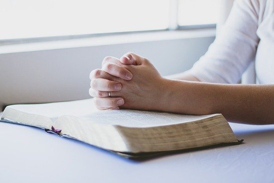 A woman with her hands folded over her Bible, praying to understand the will of God