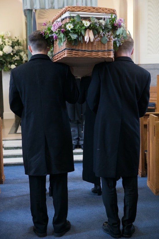 Two men in black suits carrying a casket of a dead person