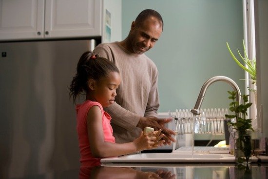 A father instructing his daughter on how to wash her hands