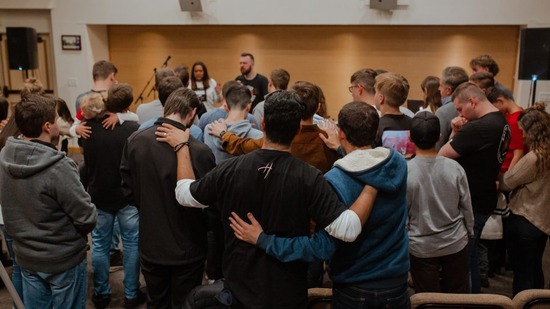 Worshippers in a church hall gathered together embracing in Sabbath fellowship and prayer.