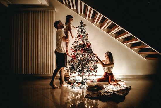A mother, father, and daughter decorating a Christmas tree by candlelight