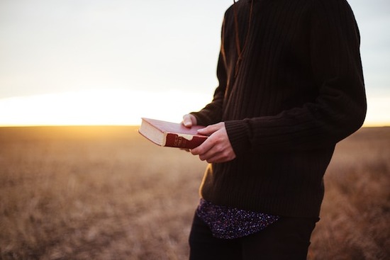 A man holding a Bible while walking in a field at sunset