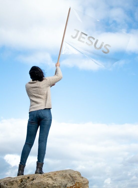 A Christian standing on a rock and waving a flag that says, Jesus