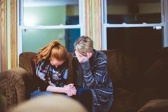 Two women bow their heads in prayer as they seek the Lord's guidance.