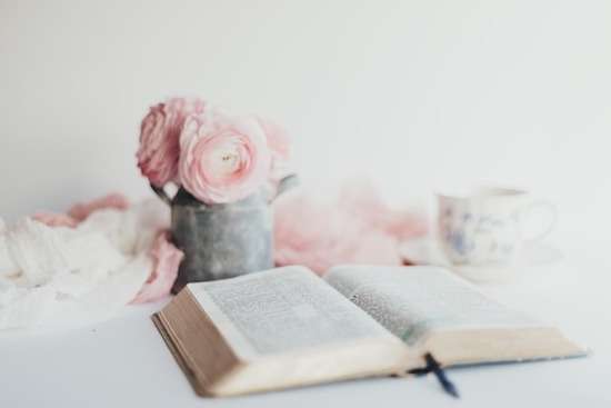An open Bible on a desk with flowers and a mug