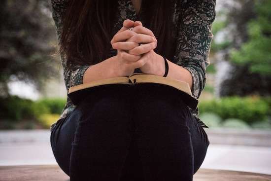 A woman with hands folded on top of a Bible