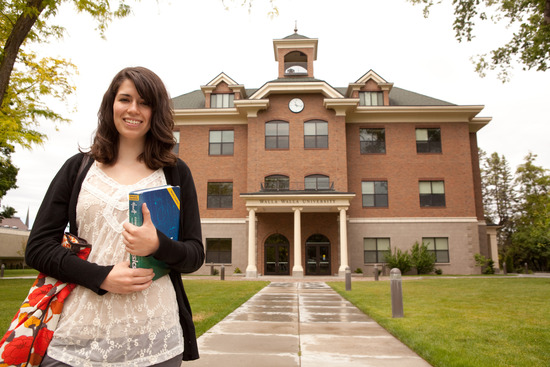 A young woman holding books and standing outside a building at Walla Walla University