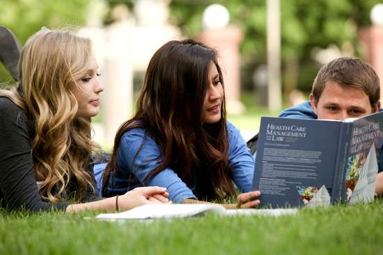 Adventist students laying on the lawn and studying a textbook