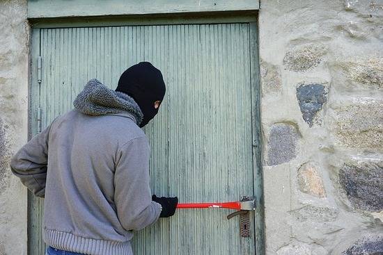A thief trying to break into a building with a crowbar