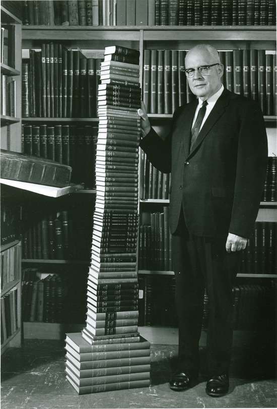 Arthur White standing next to a stack of books written by Ellen White