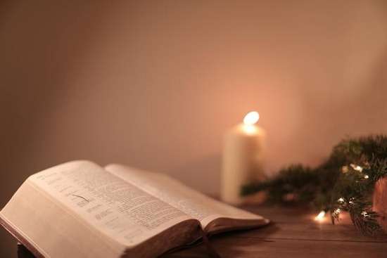  A Bible open with Christmas lights and candles surrounding it