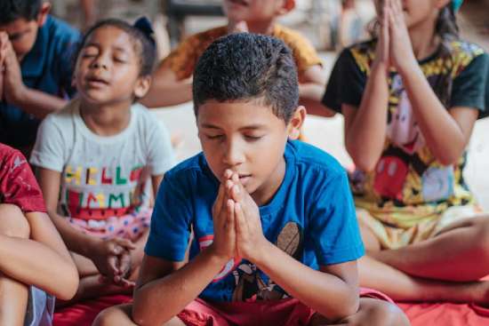 Children with hands folded and eyes closed in prayer during sabbath school
