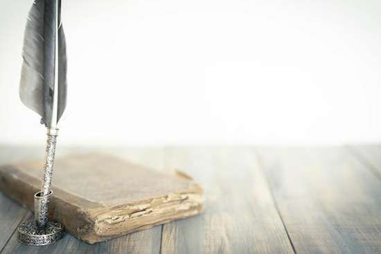 An old book next to a feather quill pen