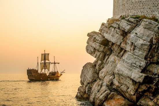 A ship of James sailing on the water near a rocky cliff