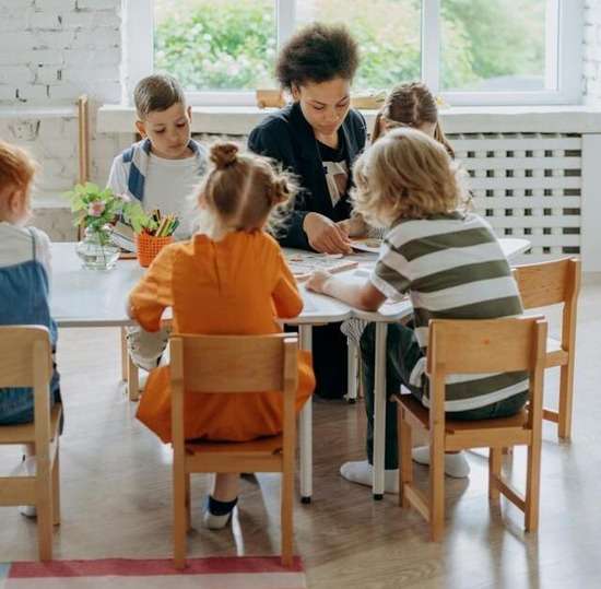 A woman sitting at a table with children and instructing them during sabbath school