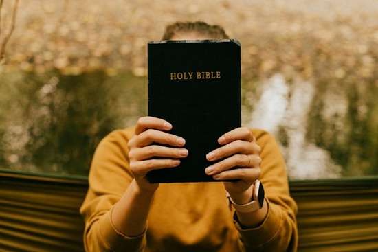 A woman holding up a Bible in front of her face