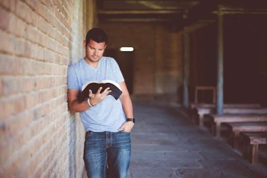 A man leaning against a wall and reading the book of Mark in the Bible