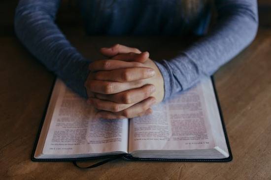 Hands folded on top of a Bible