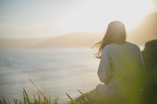 A woman sitting on a hill and looking out on the ocean