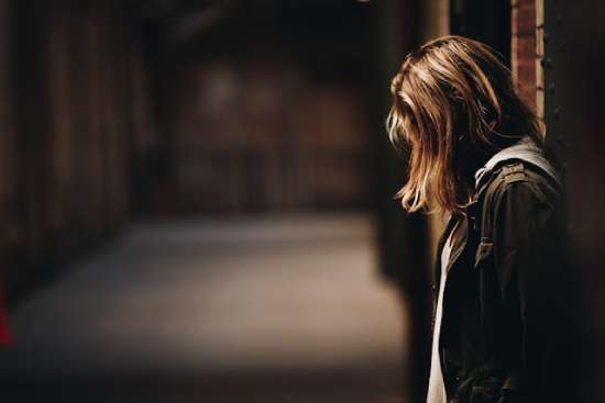 A woman leaning against a wall and bowing her head in discouragement