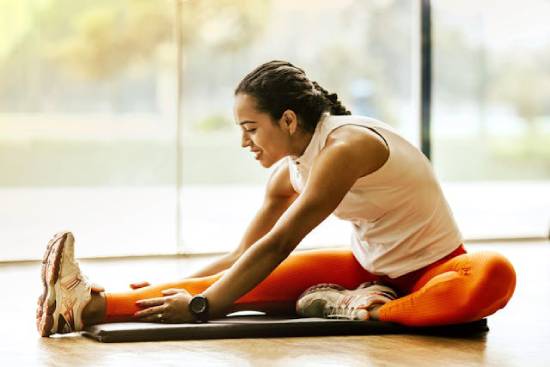 Woman stretching on the floor A woman stretches her leg while sitting on the floor, demonstrating fitness as a necessary part of our health.