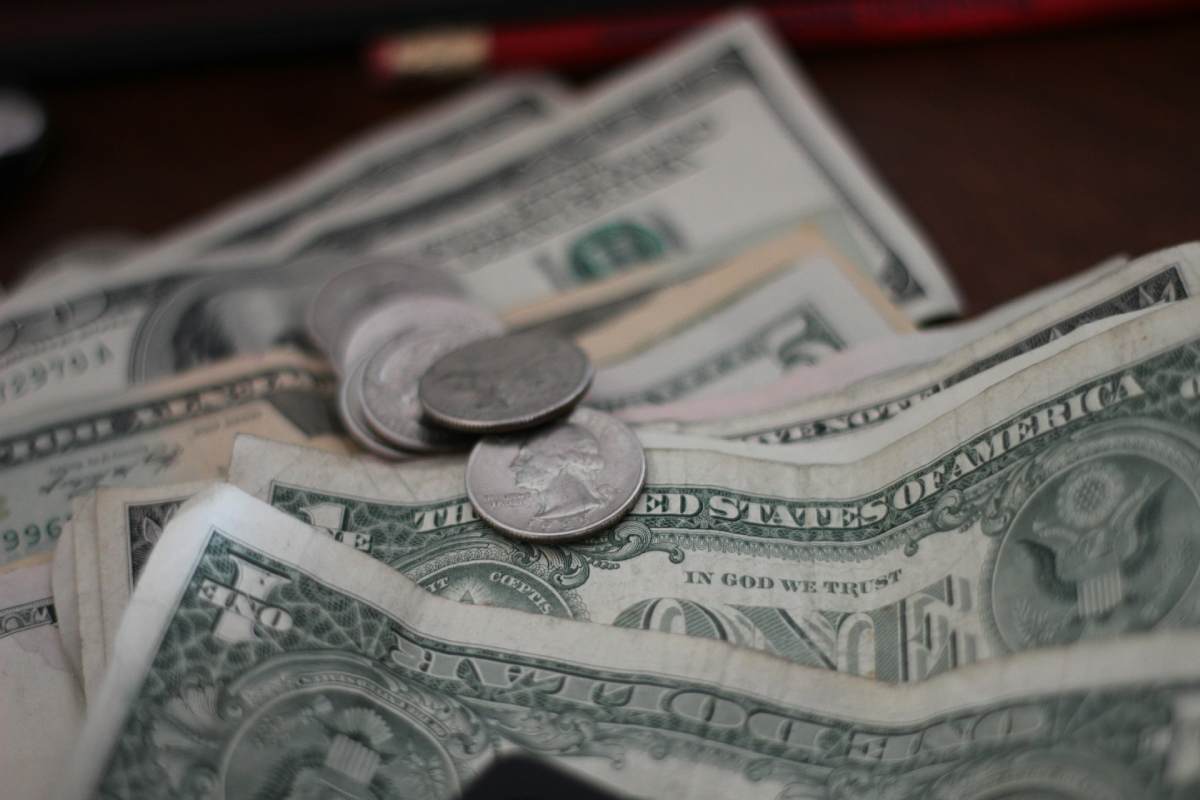 A hand places a folded $1 bill into a cross-shaped slot, signifying that a small portion of our income should be dedicated to God, as He provided the ultimate sacrifice for us.