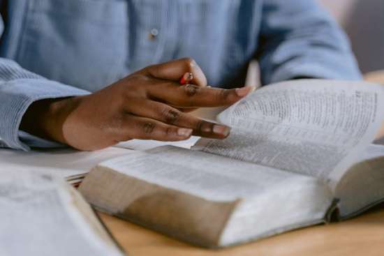 Woman Reading her Bible with a Coffee A person flipping through a Bible, pencil in hand