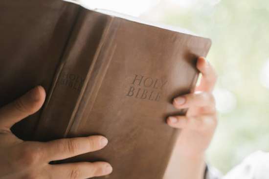 Person Holding Open a Brown Leather Bible A person holding open a brown leather Bible as they read