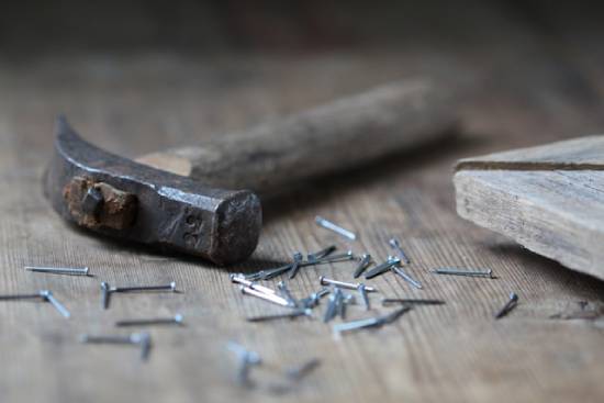 A hammer and nails on some distressed wood A hammer rests on a wooden floor amidst a pile of nails