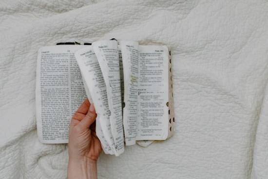 Someone sits on a bed and flips through the Bible.