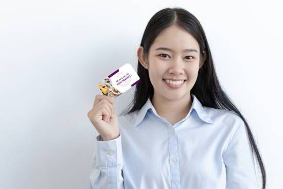 A young woman smiles while holding up an Ask An Adventist Card in her hand.