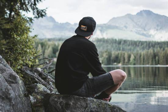 A man sitting on a rock by a lake, enjoying a relaxing moment in nature.