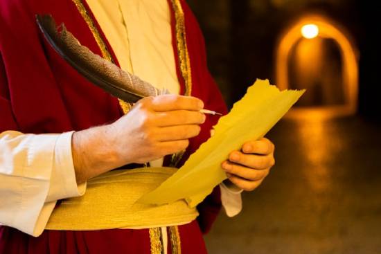Man holding a feather pen and parchment An ancient scribe makes notes on parchment paper with his quill.