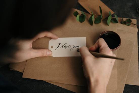 Man's hands writing "I love you" with a pen on a paper tag Someone writes