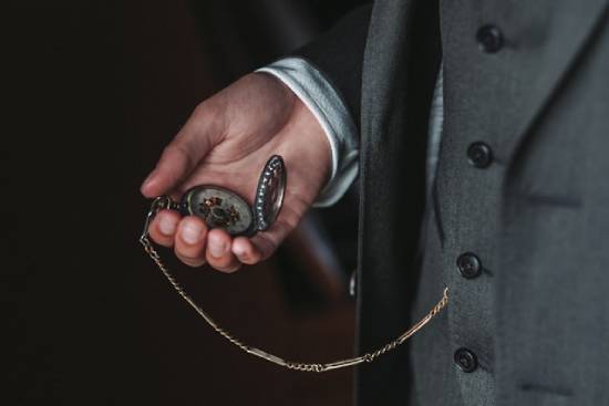A man in a fancy suit looks at his vest pocket watch