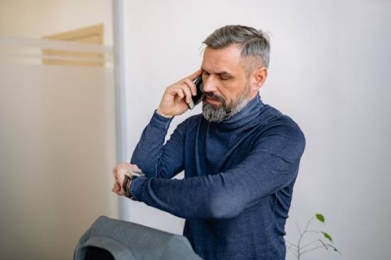 A businessman talks on his cellphone while impatiently checking his watch.