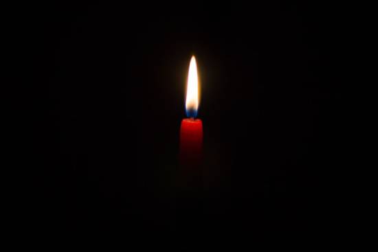 Red lit candle against a black background A lit candle in the dark.