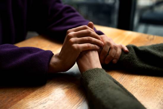 Two people clasping hands as a gesture of forgiveness Two people grasp hands across a table.