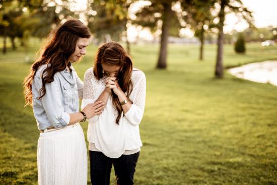 Two women praying for forgiveness Two young women pray together in an open field.