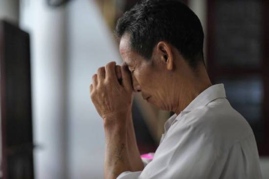 Man praying indoors A man clasping his hands and closing his eyes in prayer