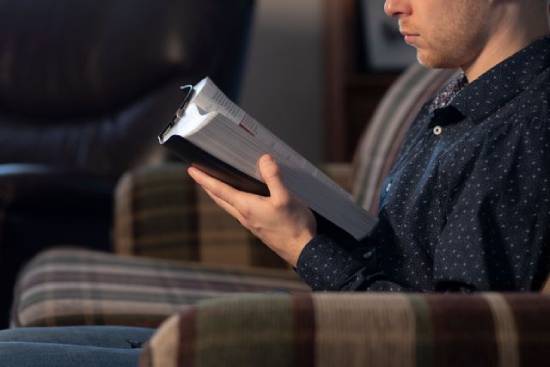 Man reading his Bible A man sits on a couch reading the Bible.