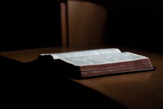 An open Bible on top of a desk An open Bible sits on a wooden table.