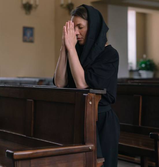 Woman praying in a church with her head covered A woman in a head covering kneels and prays in a church.